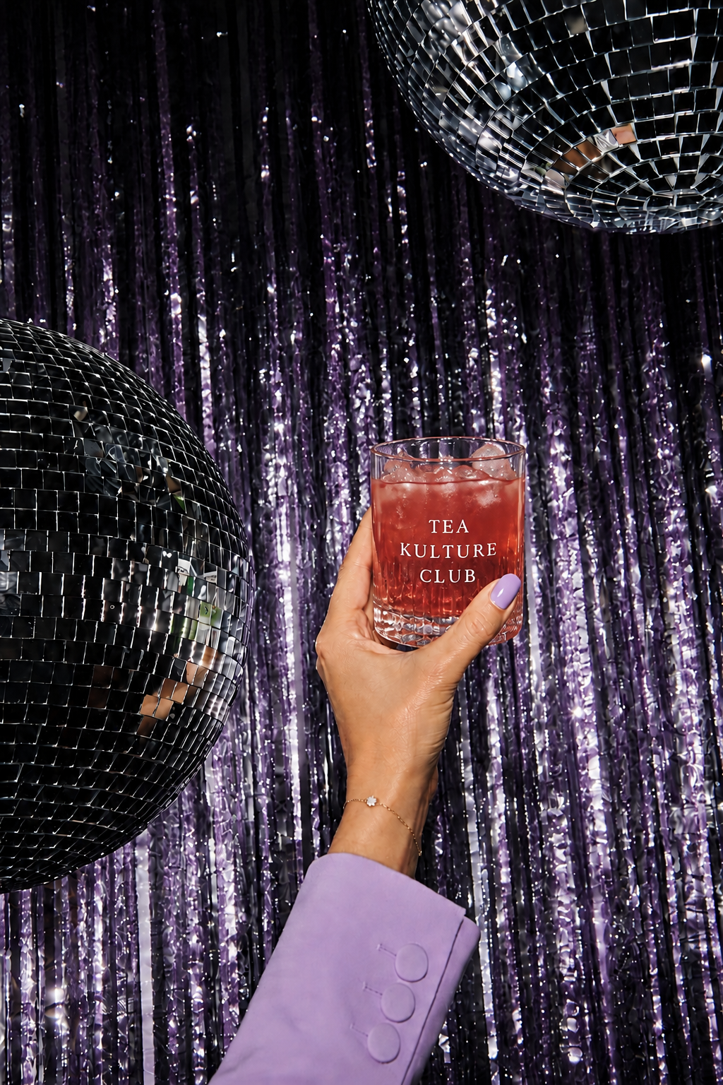Hand holding a Tea Kulture Club iced tea against a purple disco ball party backdrop